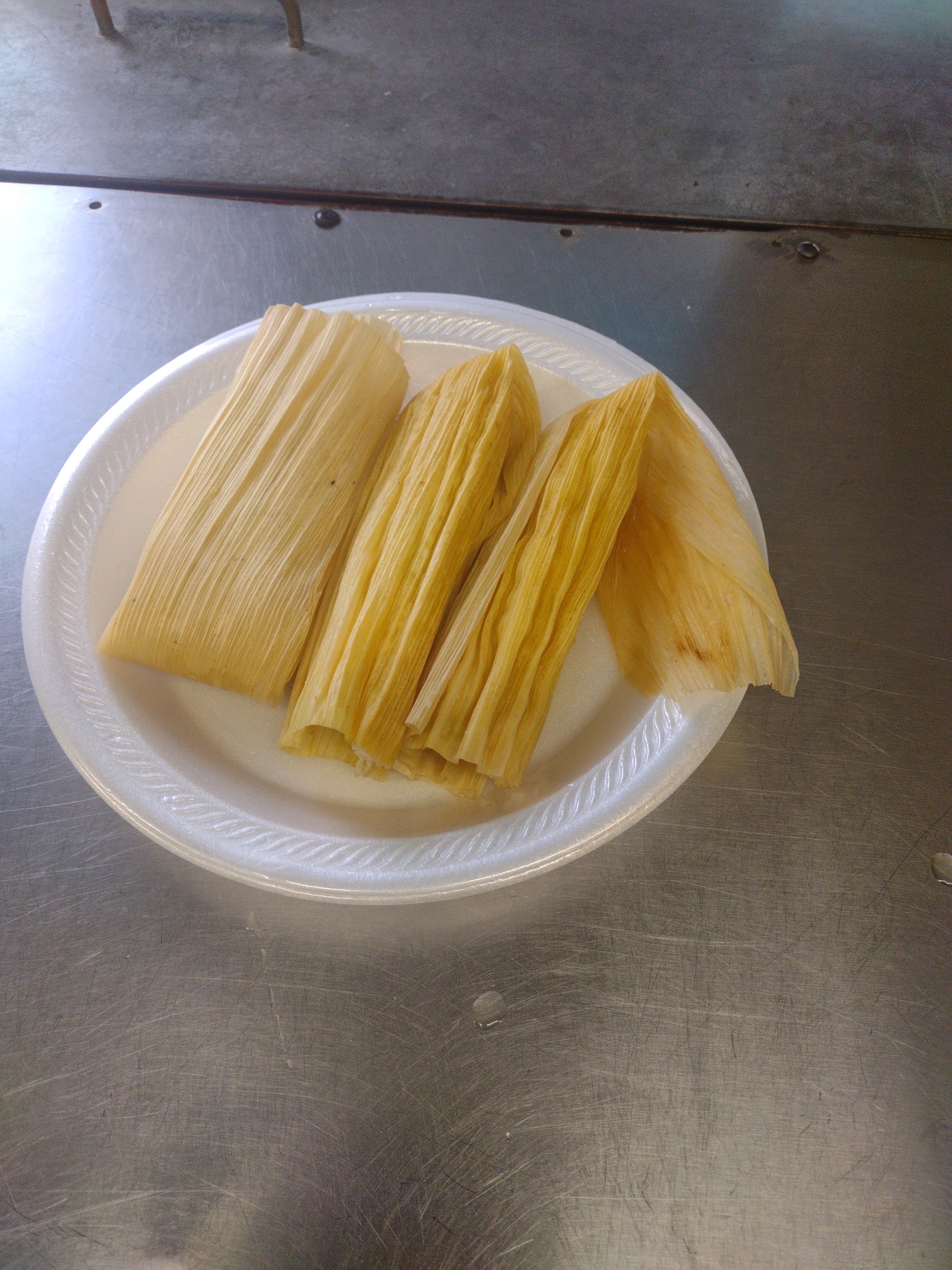 Three tamales in corn husks on a plate