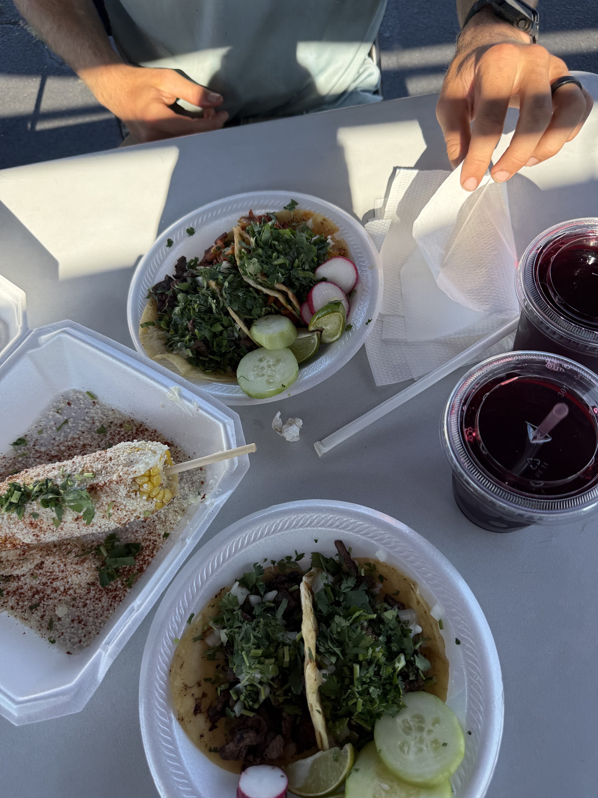 Tacos, elote and two glasses of agua de jamaica on a table outside