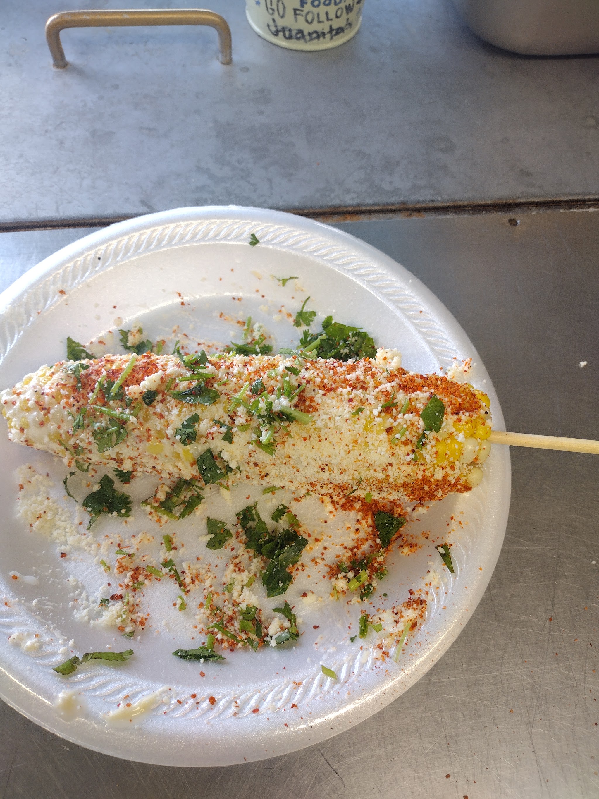 Elote, grilled street corn with cheese, chili and cilantro, on a foam plate