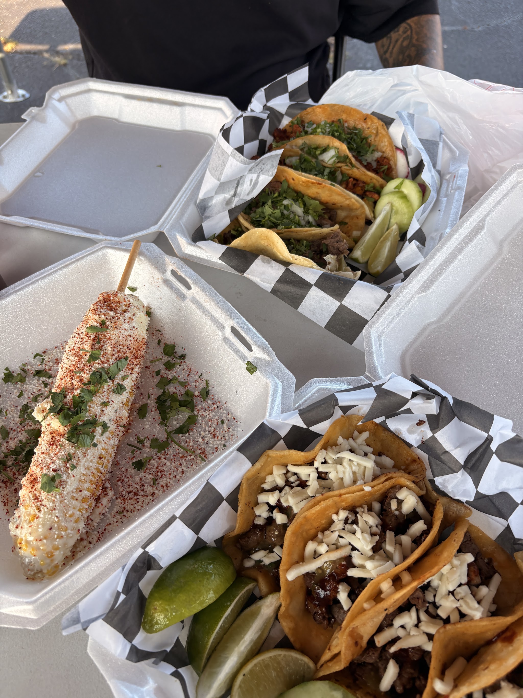 Street tacos with cilantro, radish and lime beside elote and two glasses of agua de jamaica